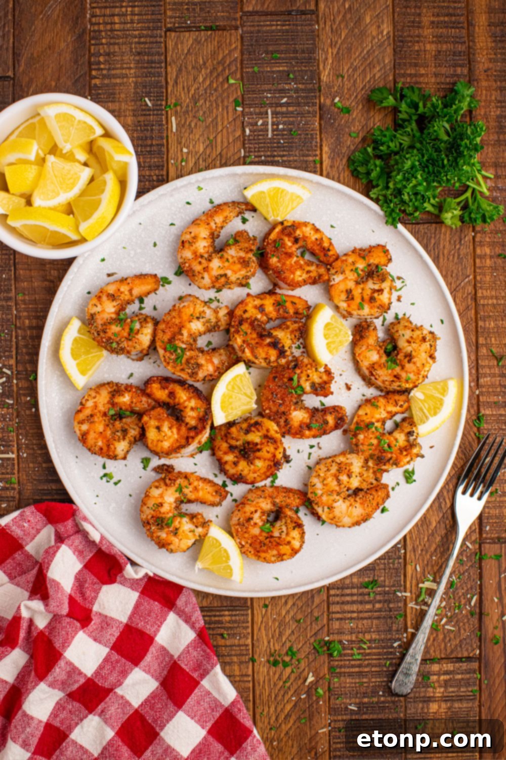 A vibrant platter of Cajun grilled shrimp, artfully arranged with fresh lemon wedges, a bowl of lemons, and sprigs of green herbs, creating an inviting presentation.