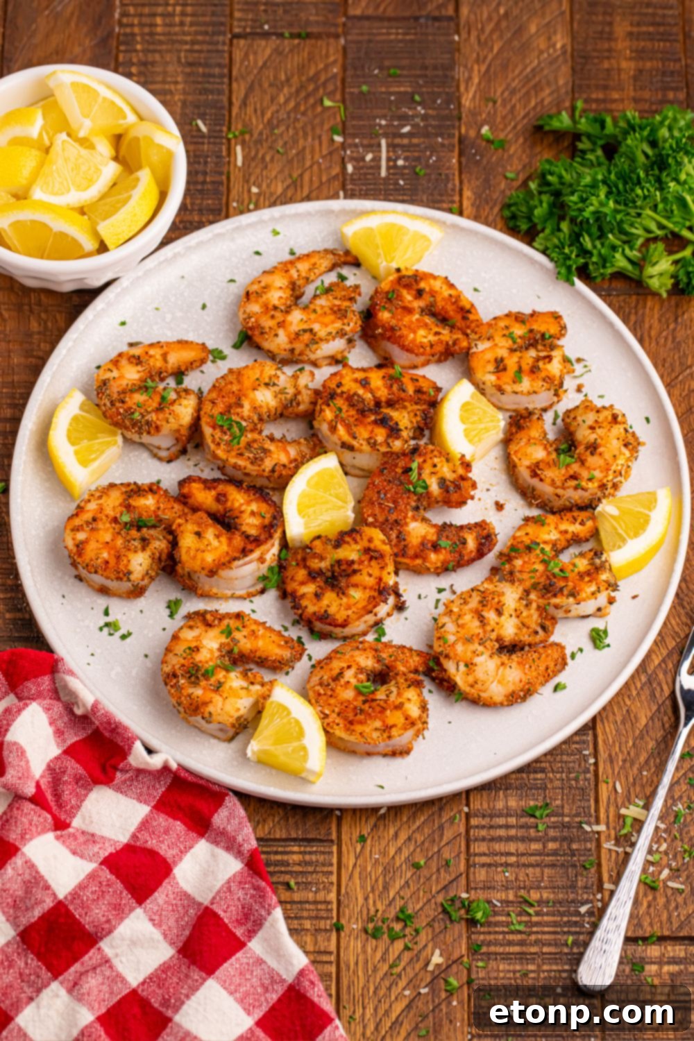 Artfully arranged Cajun grilled shrimp on a white plate, garnished with fresh lemon wedges and a sprinkle of green herbs, highlighting the vibrant colors and appealing texture of the cooked shrimp.