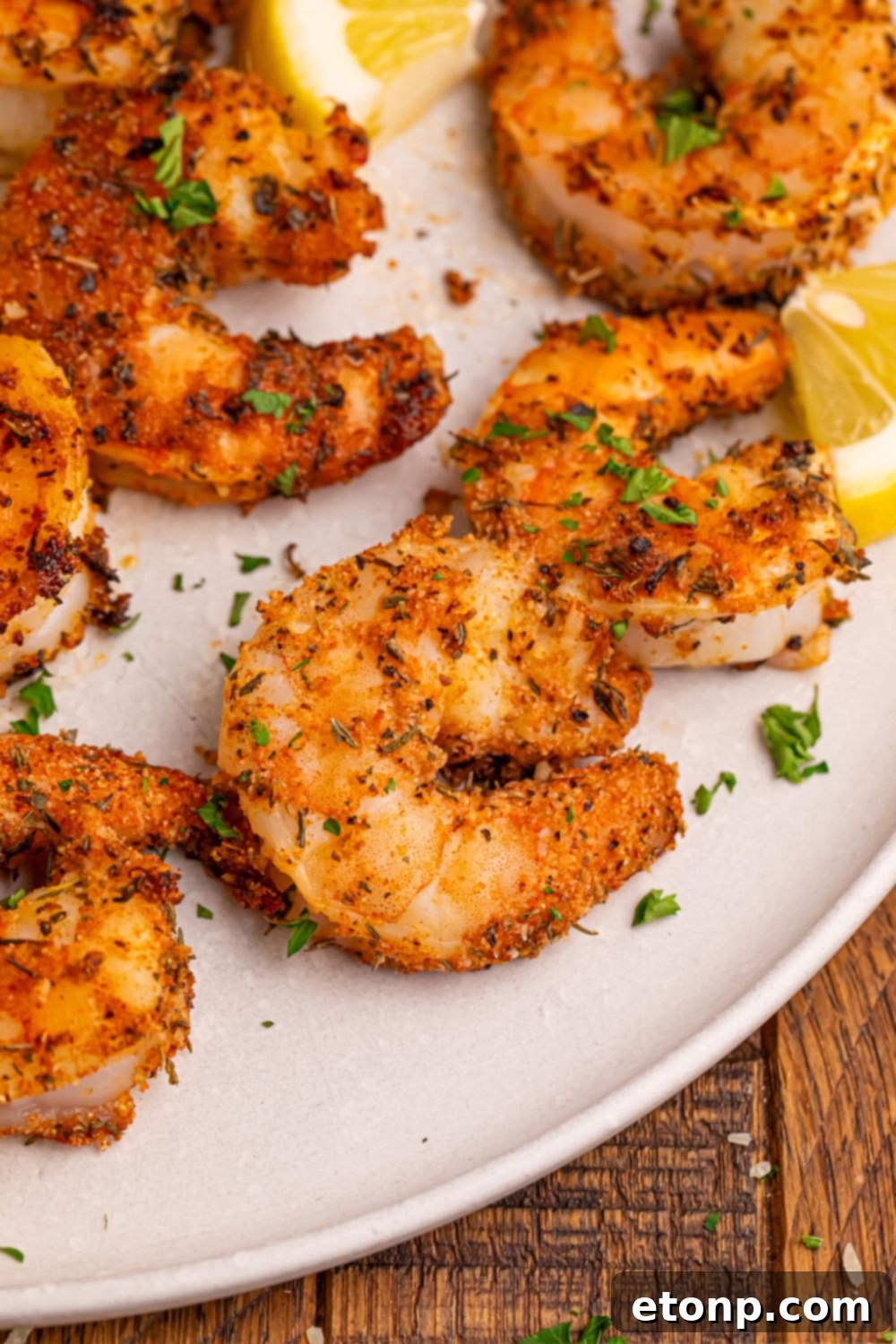 Uncooked large raw shrimp generously coated with a vibrant Cajun spice blend, ready for grilling, displayed on a plate with fresh lemon slices.