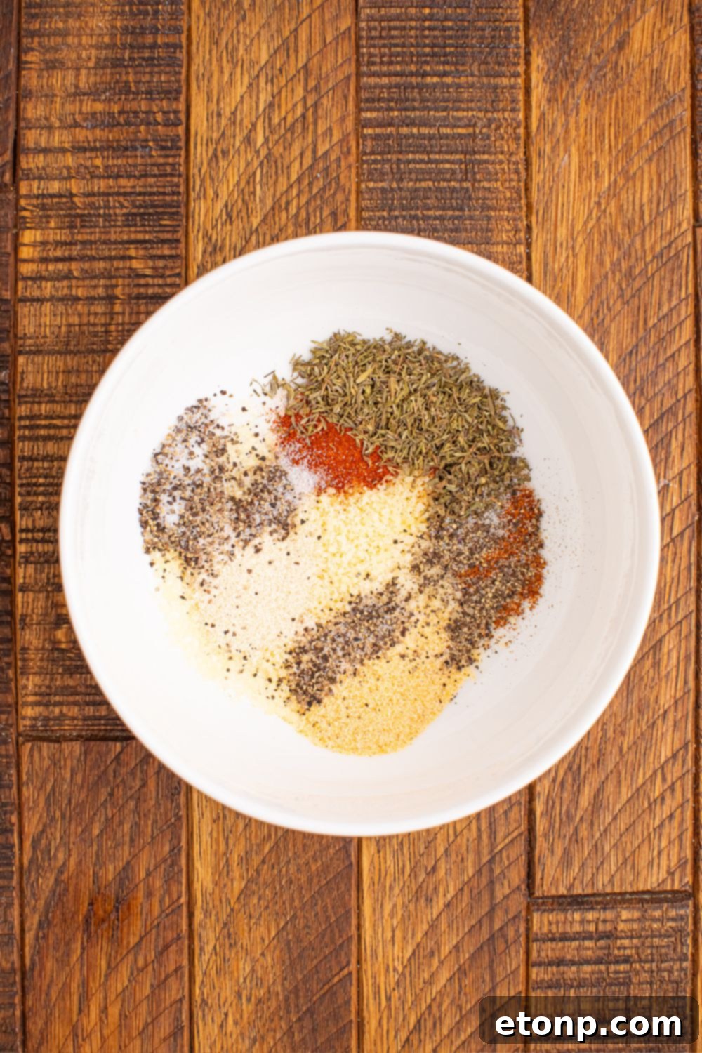 A small bowl filled with the vibrant homemade Cajun spice blend, showcasing the rich colors of the garlic powder, onion powder, thyme, paprika, basil, black pepper, salt, and cayenne pepper.