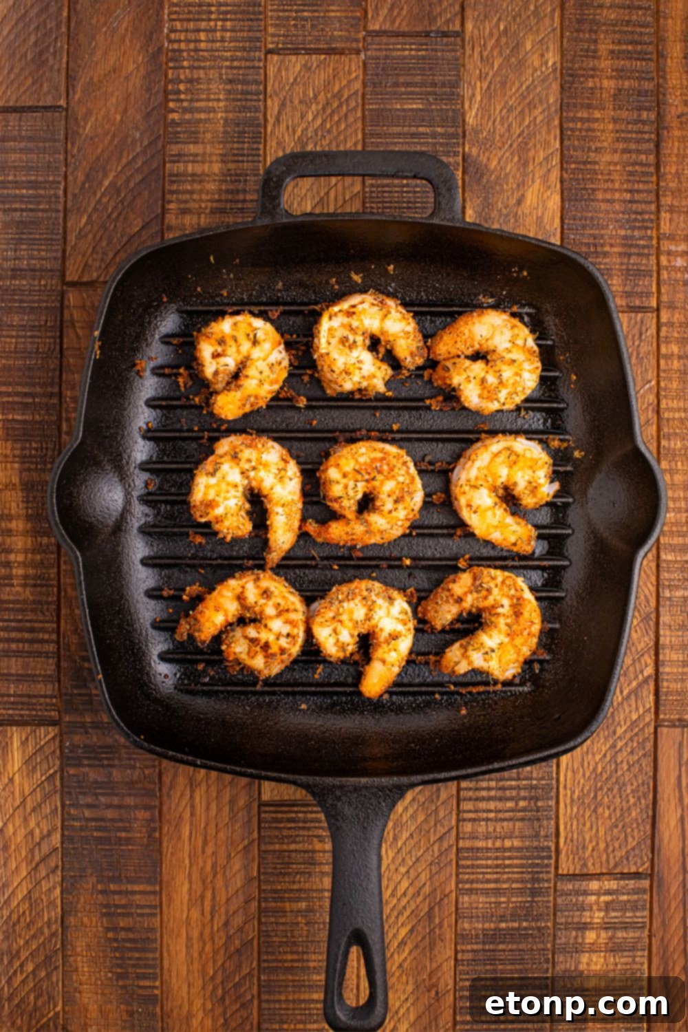 Close-up view of Cajun seasoned shrimp sizzling on a hot grill pan, showcasing the delicious crust forming on the seafood.
