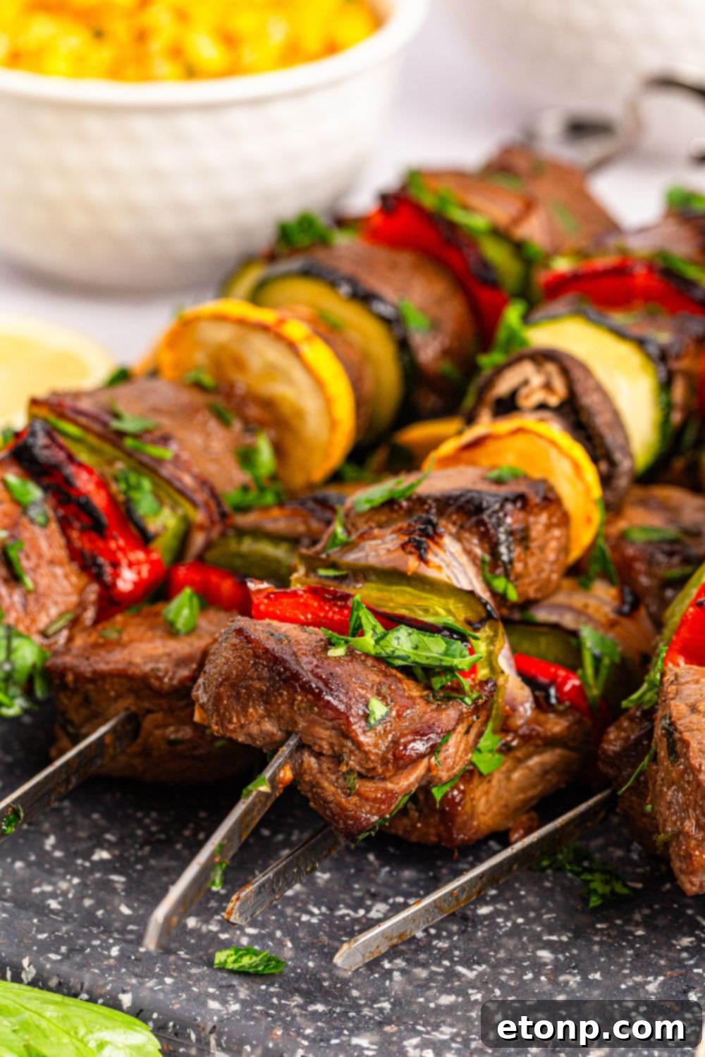 Marinated Beef Kabobs on a metal tray with a bowl of corn in the background 