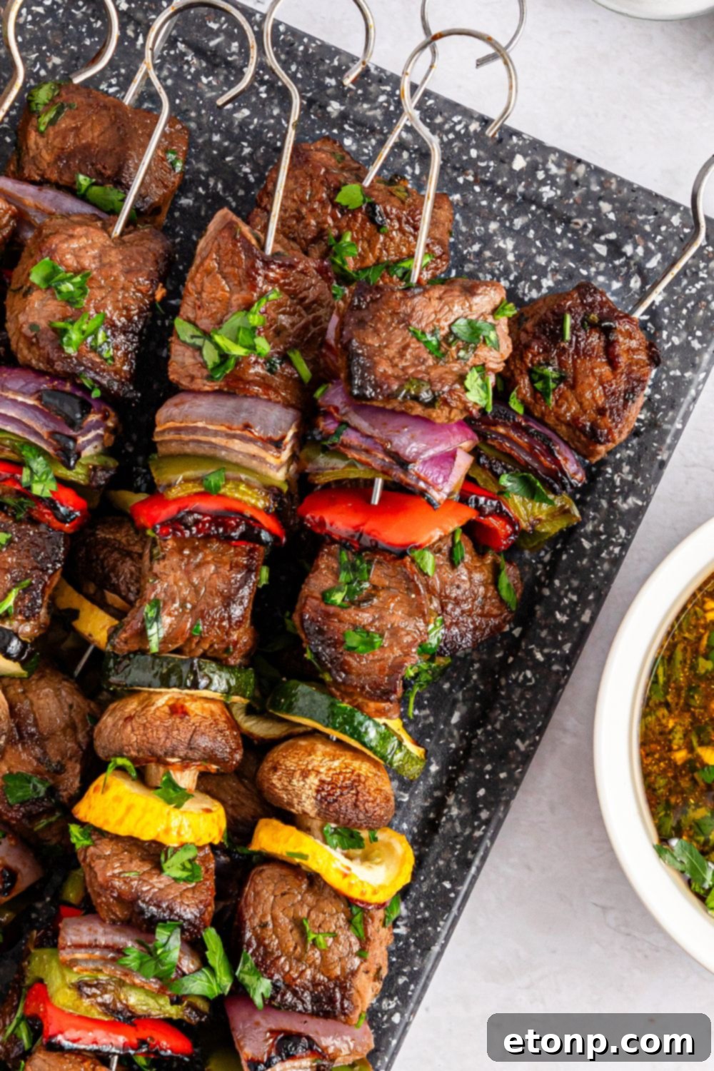 beef skewers with vegetables sitting on a tray with a bowl of extra marinade on the side