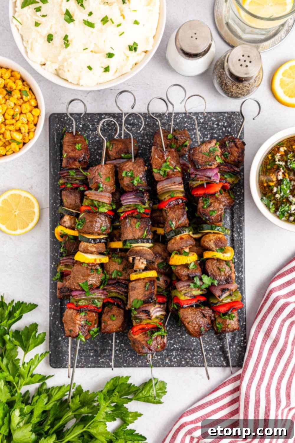 overhead look of Marinated Beef Kabobs on a tray with parsley, a bowl of corn, mashed potatoes and more all around the tray 