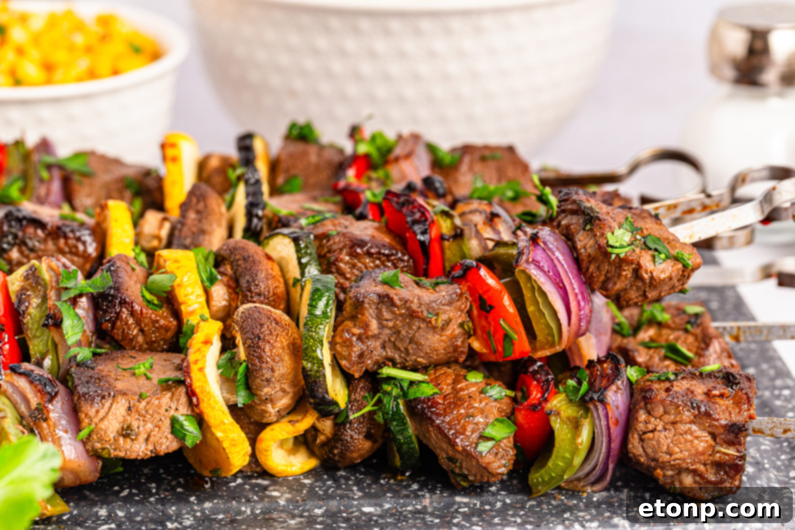 Marinated Beef Kabobs on a platter sitting on table with a bowl of corn in the background