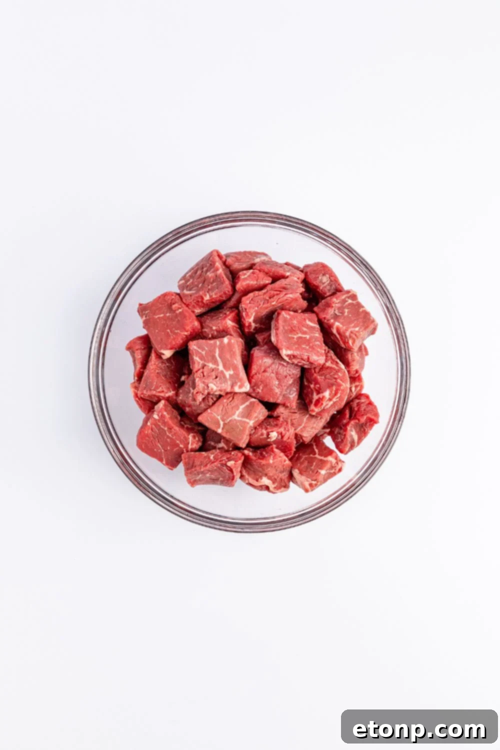 raw cubed steak in a glass bowl on white counter 