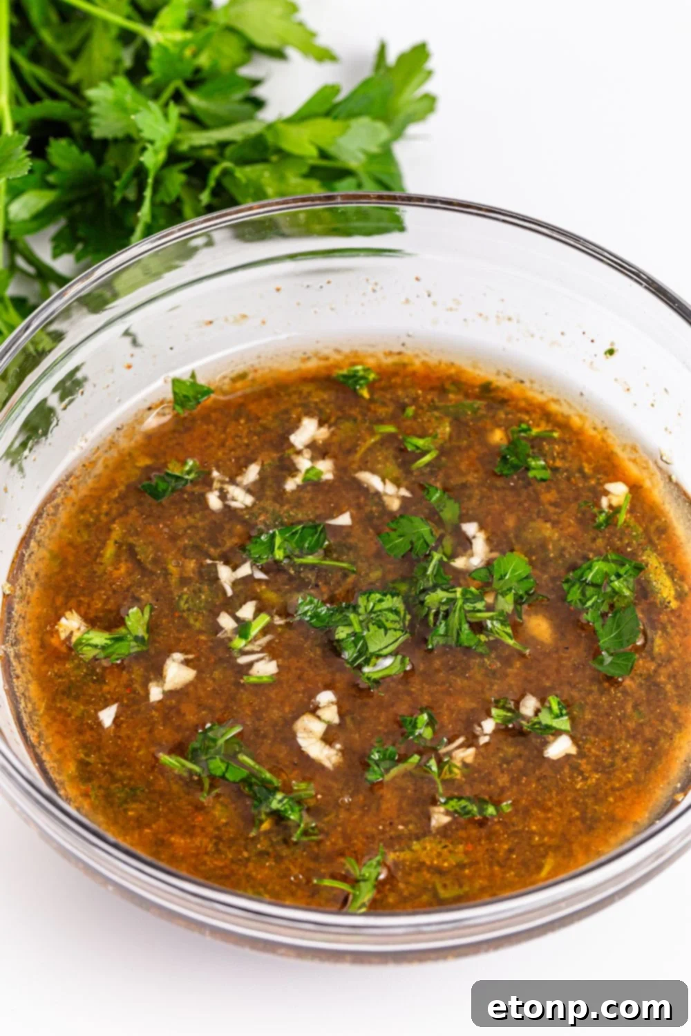 liquid marinade for Marinated Beef Kabobs in a bowl sitting on table with parsley behind it