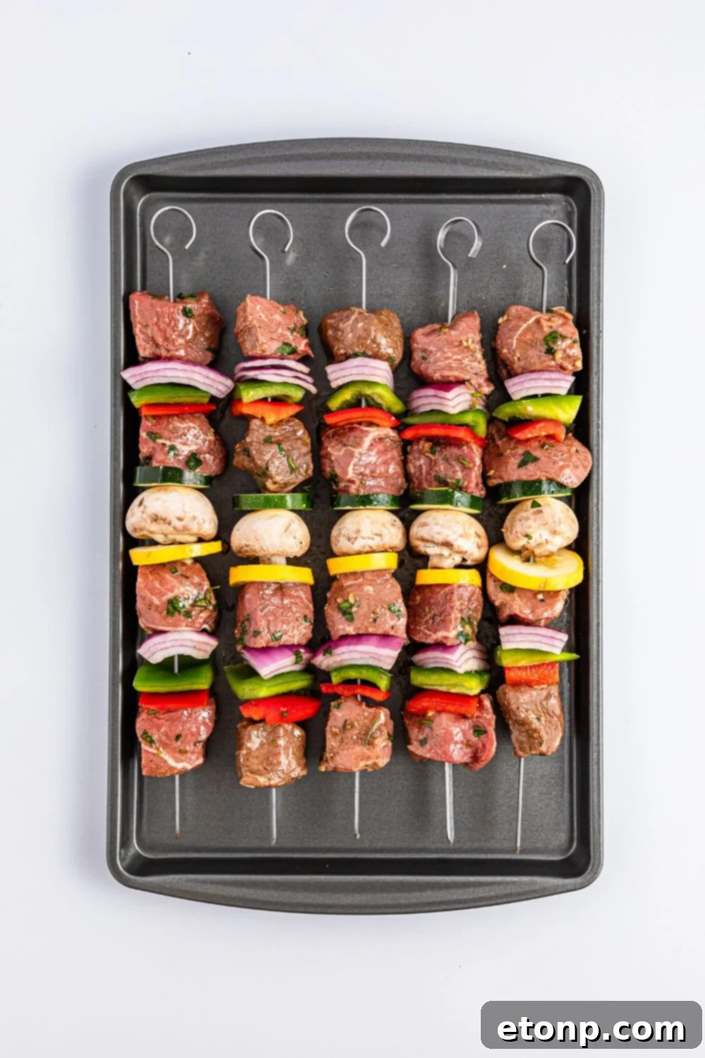 raw Marinated Beef Kabobs on a cookie sheet sitting on table 