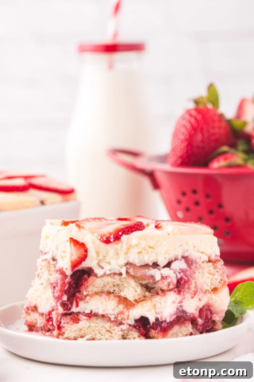 Strawberry Dream Tiramisu 12 A strainer filled with fresh strawberries, a glass of milk, and a plate with a slice of Strawberry Tiramisu.