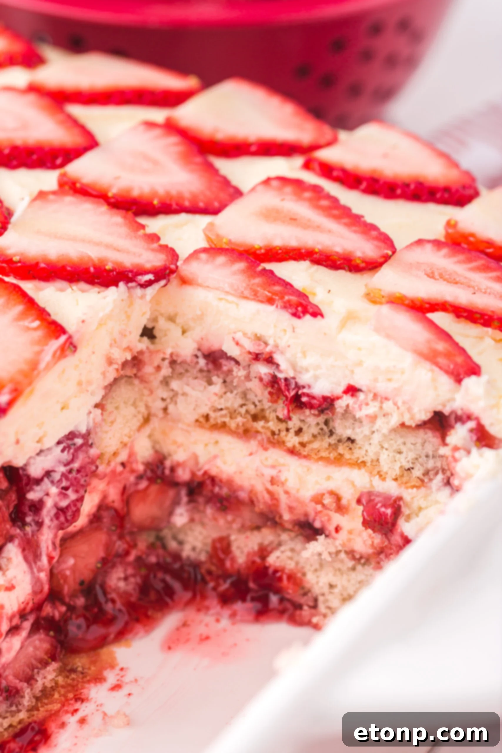 Strawberry Dream Tiramisu 16 A white baking dish containing Strawberry Tiramisu, with one slice already removed, showcasing its appealing layers.