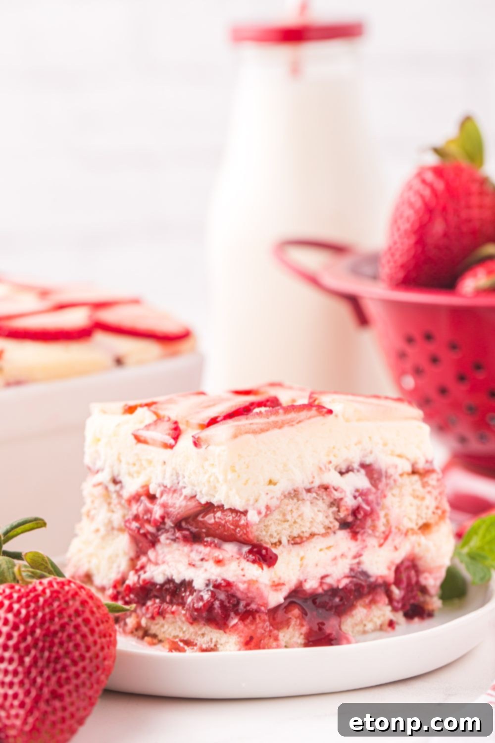 Strawberry Dream Tiramisu 4 A slice of Strawberry Tiramisu on a plate, adorned with fresh strawberries and a glass of milk in the background.