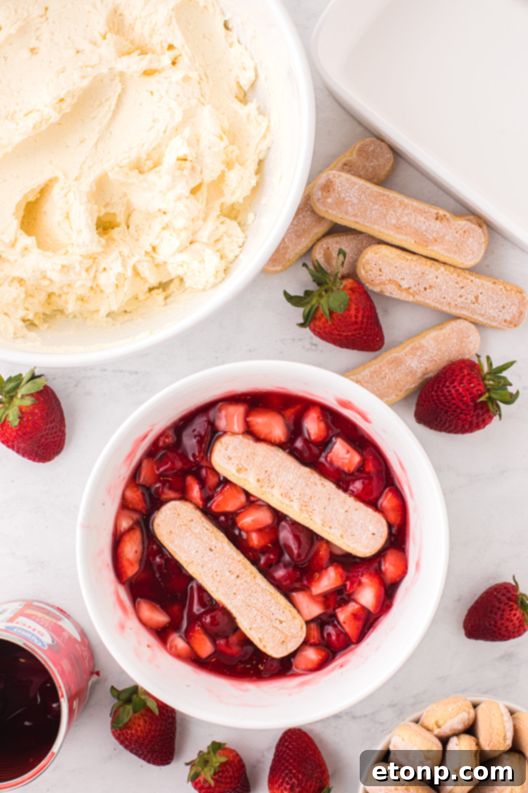 Strawberry Dream Tiramisu 7 Ladyfingers soaking in a vibrant strawberry mixture, with a bowl of creamy mascarpone filling in the background.