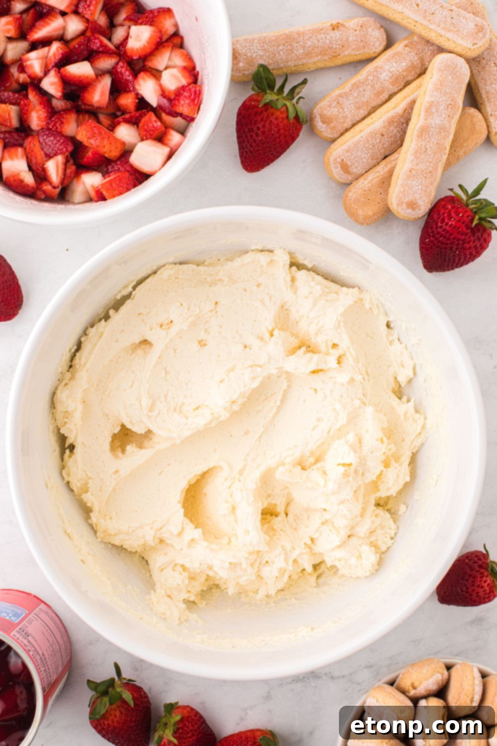 Strawberry Dream Tiramisu 8 A bowl of freshly prepared mascarpone filling, surrounded by ladyfingers and bowls of fresh berries on a rustic table.