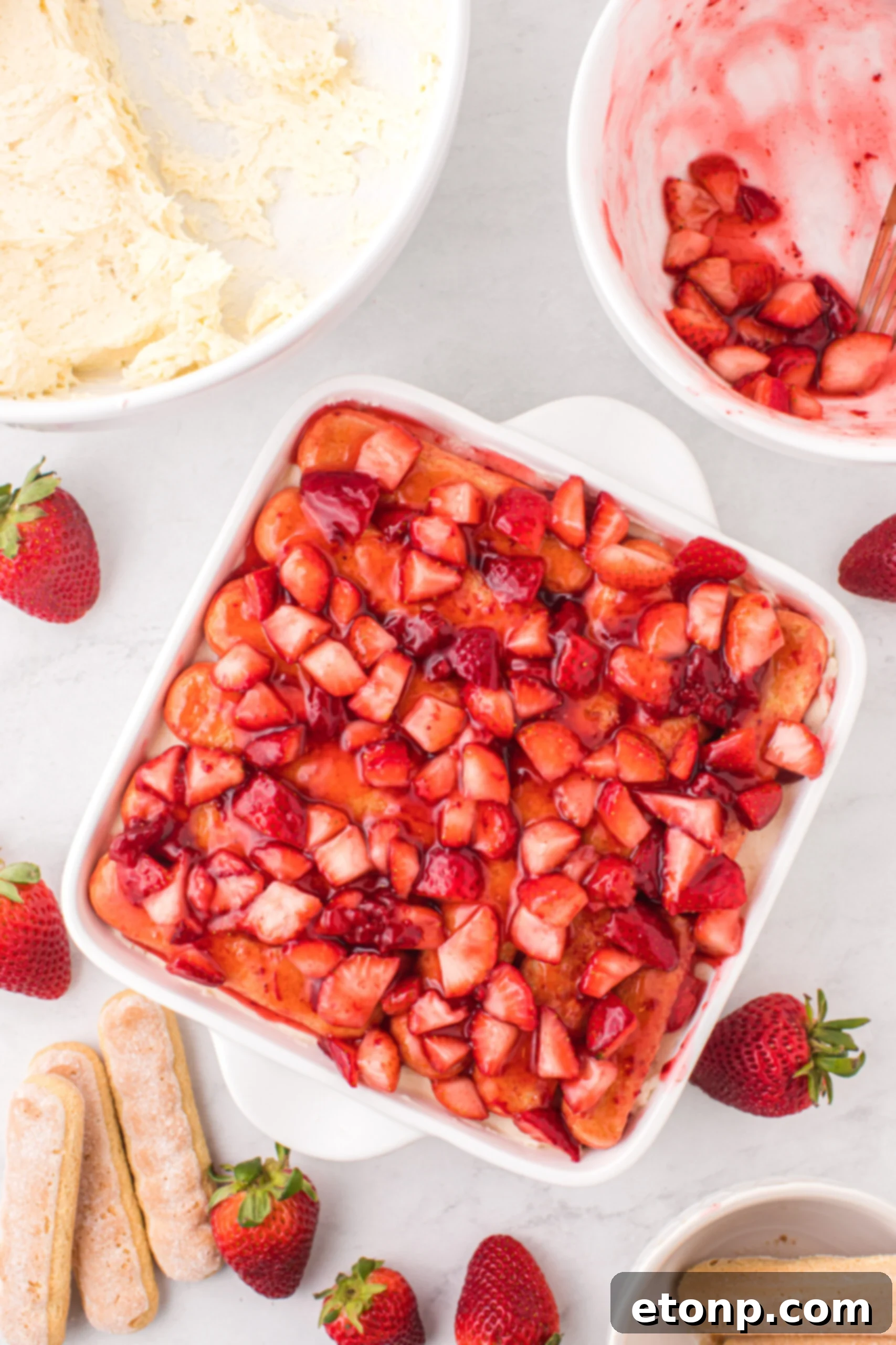 Strawberry Dream Tiramisu 10 Finished Strawberry Tiramisu in a pan on a table, next to bowls of mascarpone filling and fresh strawberries.