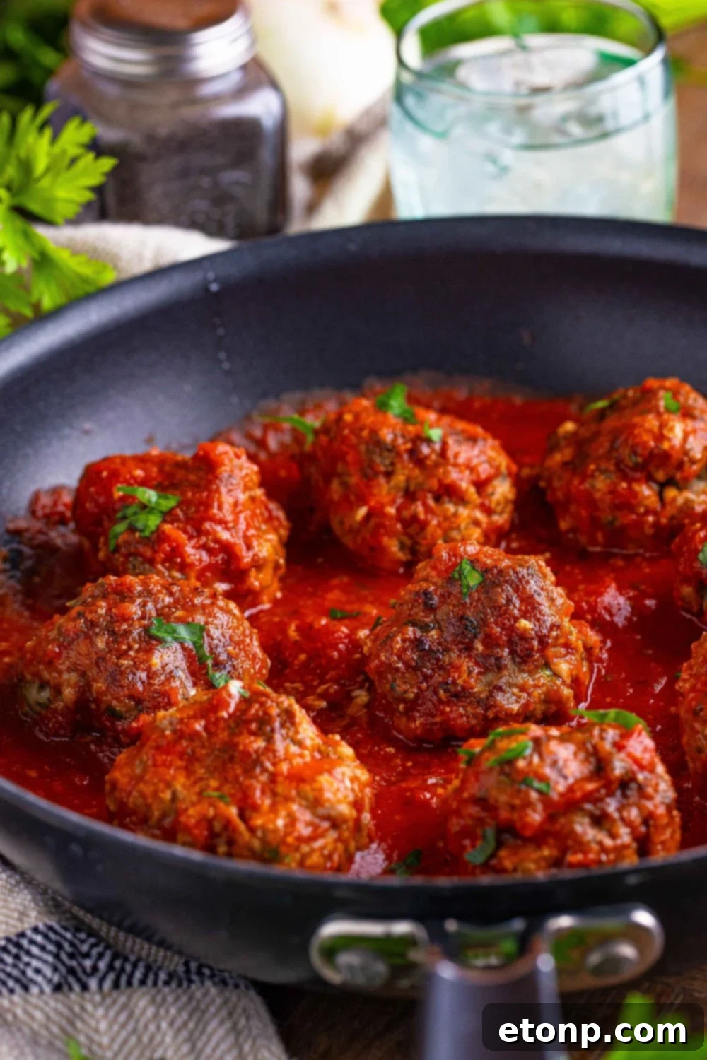 Classic Italian Meatballs in a pan that is topped with sauce and parsley 