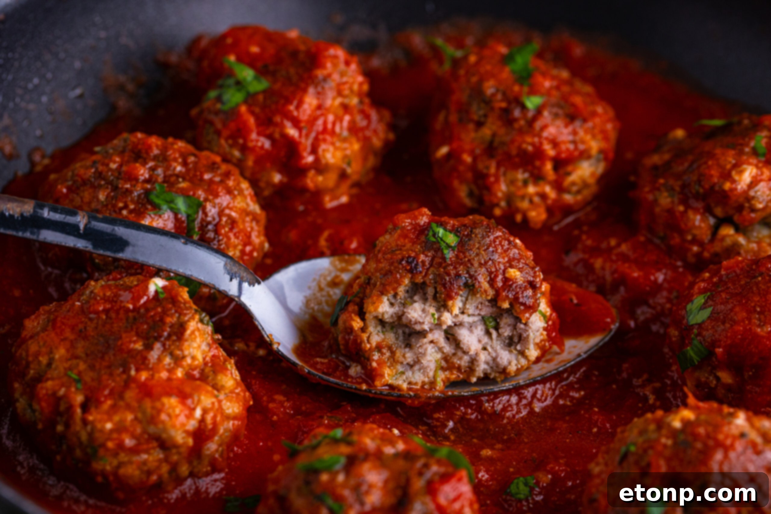 Classic Italian Meatball with a bite taken out of it close up in a pan with a marinara sauce drizzled on top 