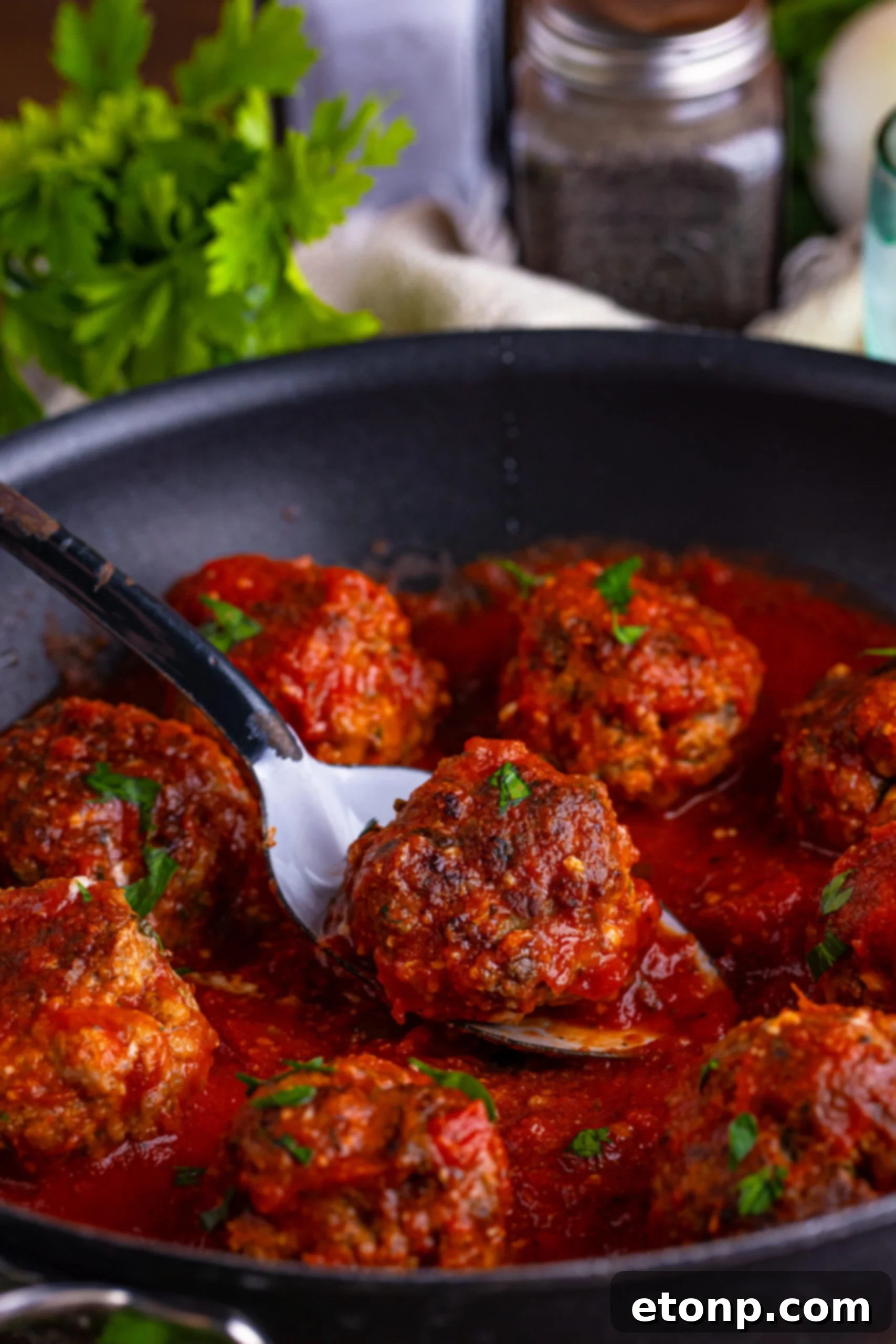 italian meatballs in a skillet with a spoon lifting one up 