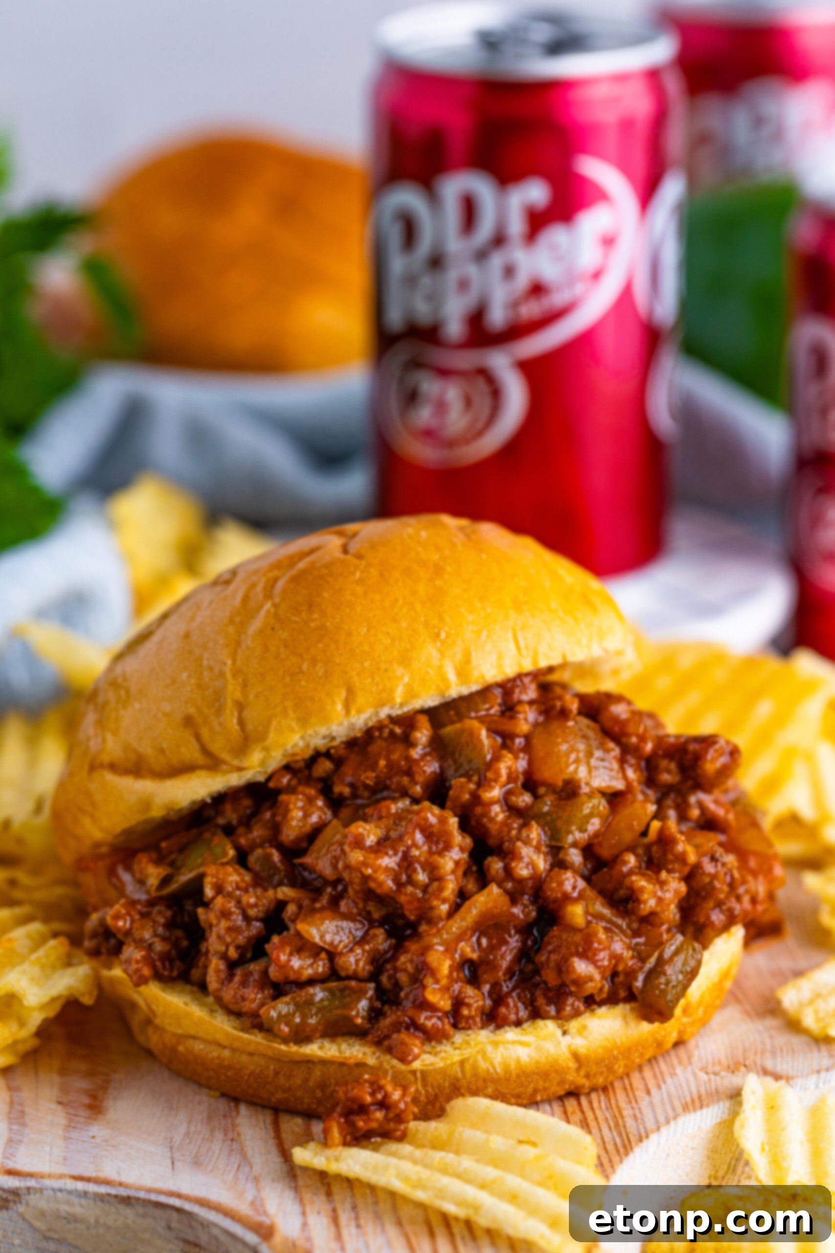 Dr. Pepper Sloppy Joe sandwich served with a side of crispy potato chips and a can of Dr. Pepper in the background, set on a rustic wooden table.