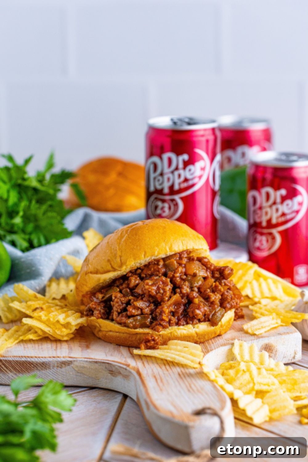 A Dr. Pepper Sloppy Joe sandwich on a cutting board, surrounded by a generous portion of potato chips and a Dr. Pepper can in the background.