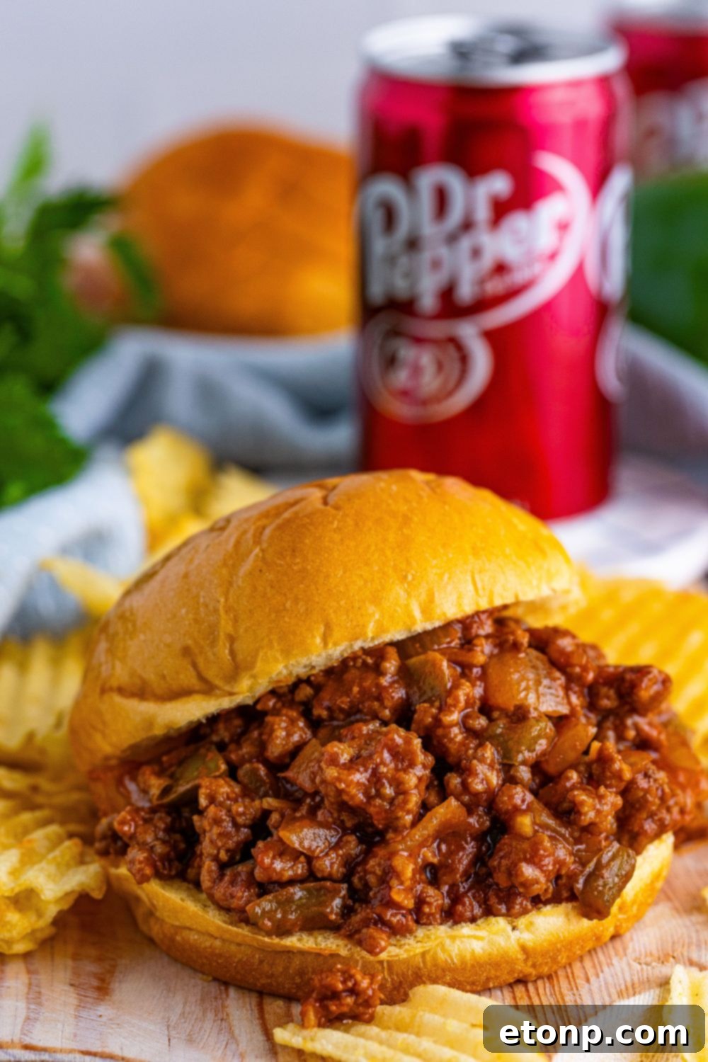 A close-up shot of Dr. Pepper Sloppy Joes served on a wooden cutting board, surrounded by golden, ruffled potato chips, highlighting the delicious meal.