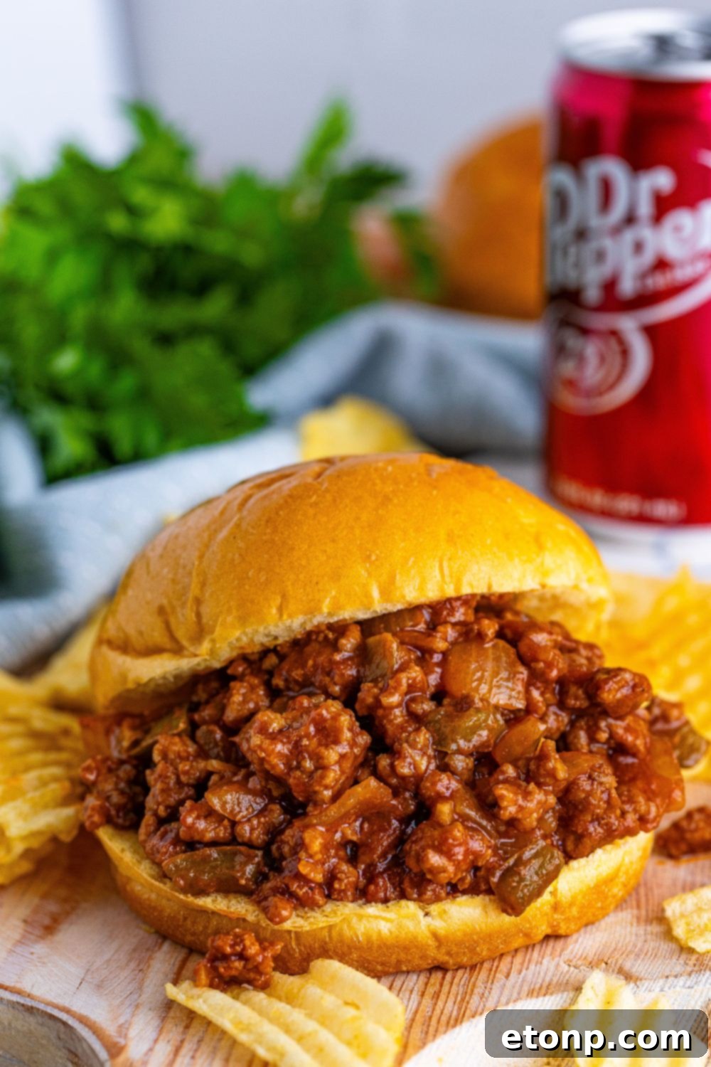 A perfectly assembled Dr. Pepper Sloppy Joe on a hamburger bun, with a scattering of ruffled potato chips around it, inviting you to take a bite.