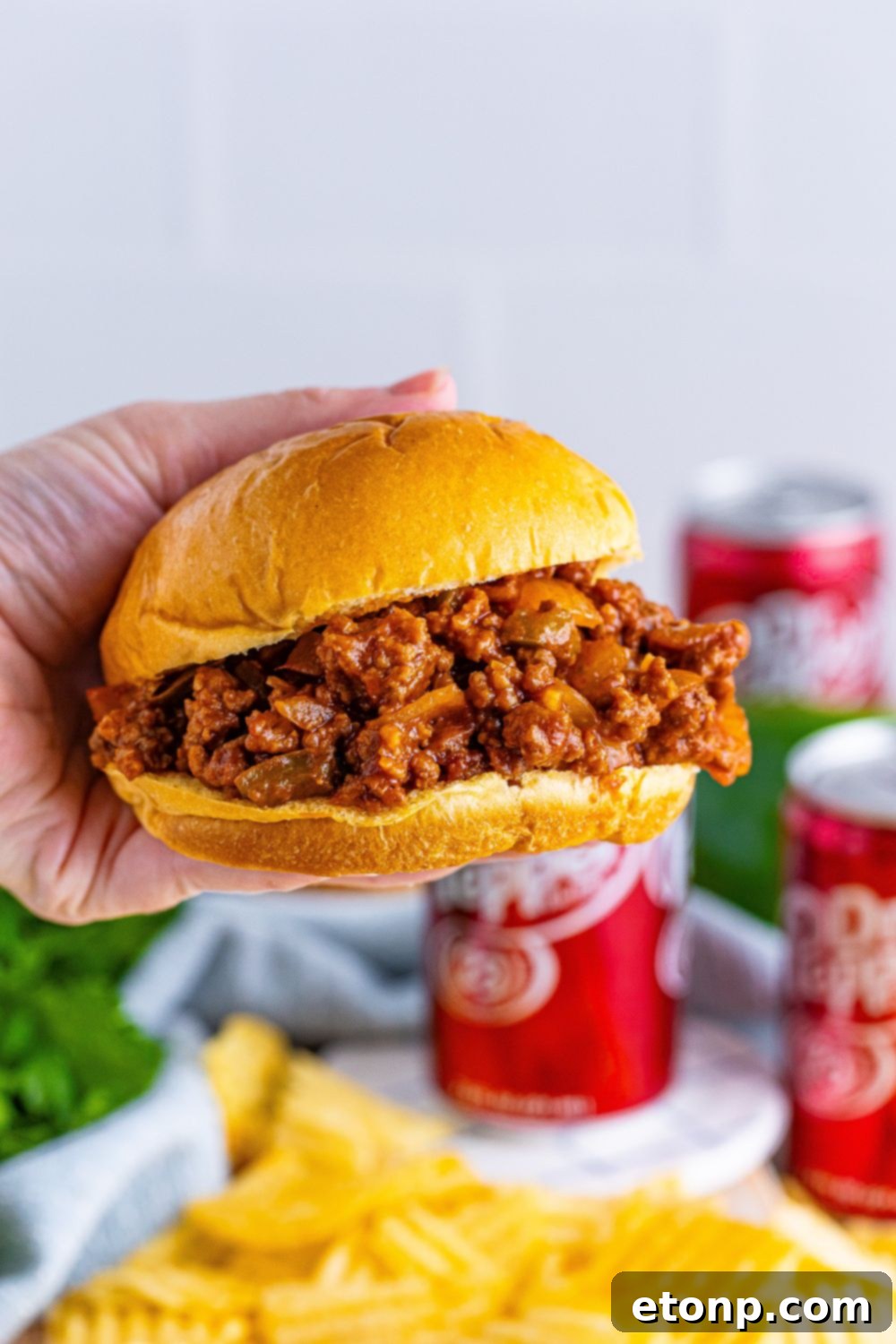 A hand holding a delicious Dr. Pepper Sloppy Joe sandwich, showcasing its hearty filling and inviting presentation.
