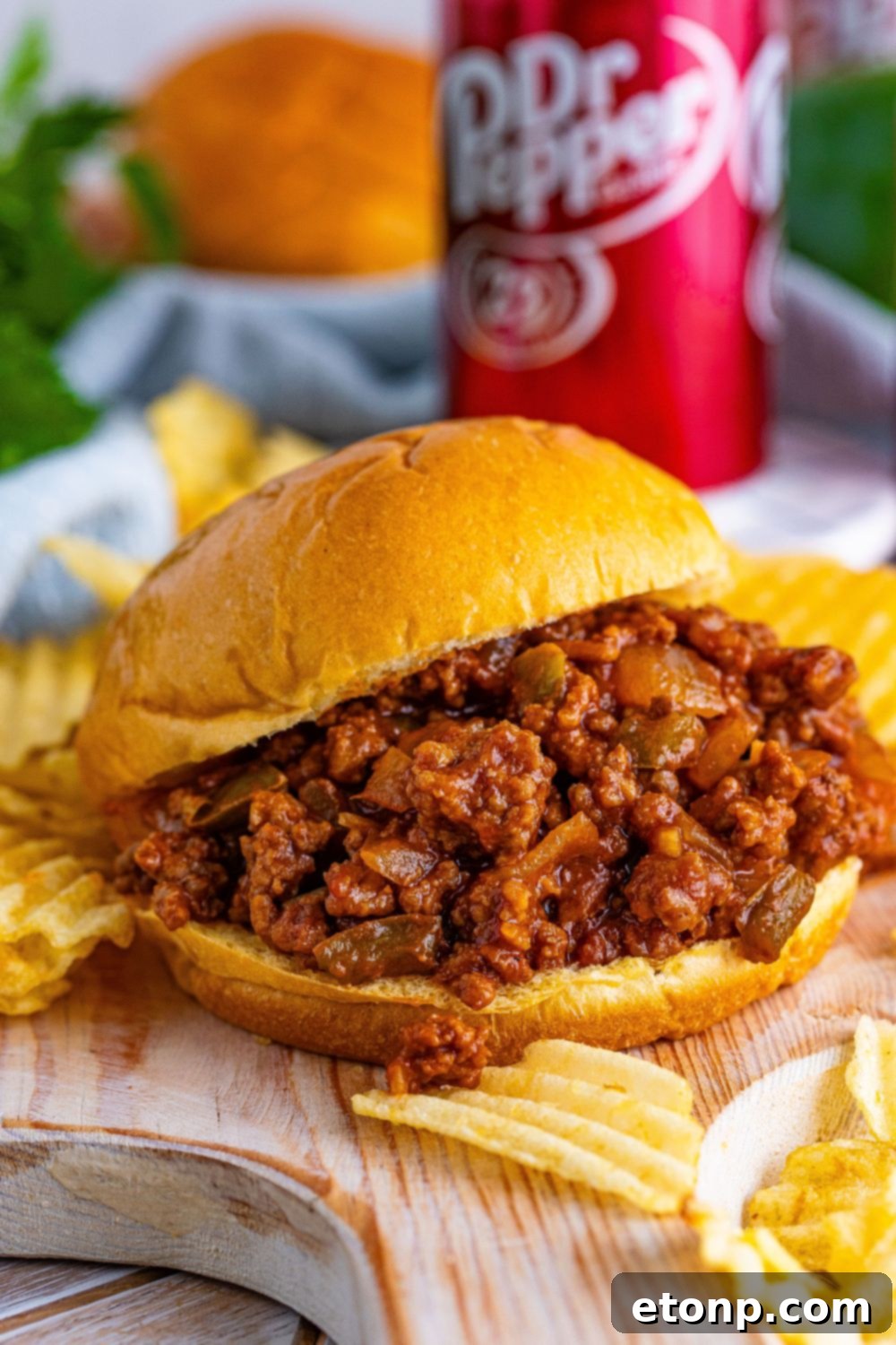 A mouth-watering Dr. Pepper Sloppy Joe sandwich resting on a wooden cutting board, with a blurred soda can in the background.