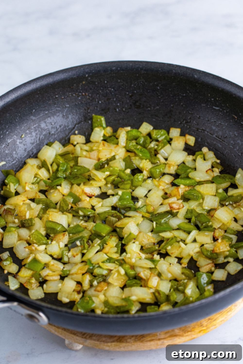 Sautéed onions and green bell peppers glistening in butter within a skillet, showing the first step of building flavor for the sloppy joes.