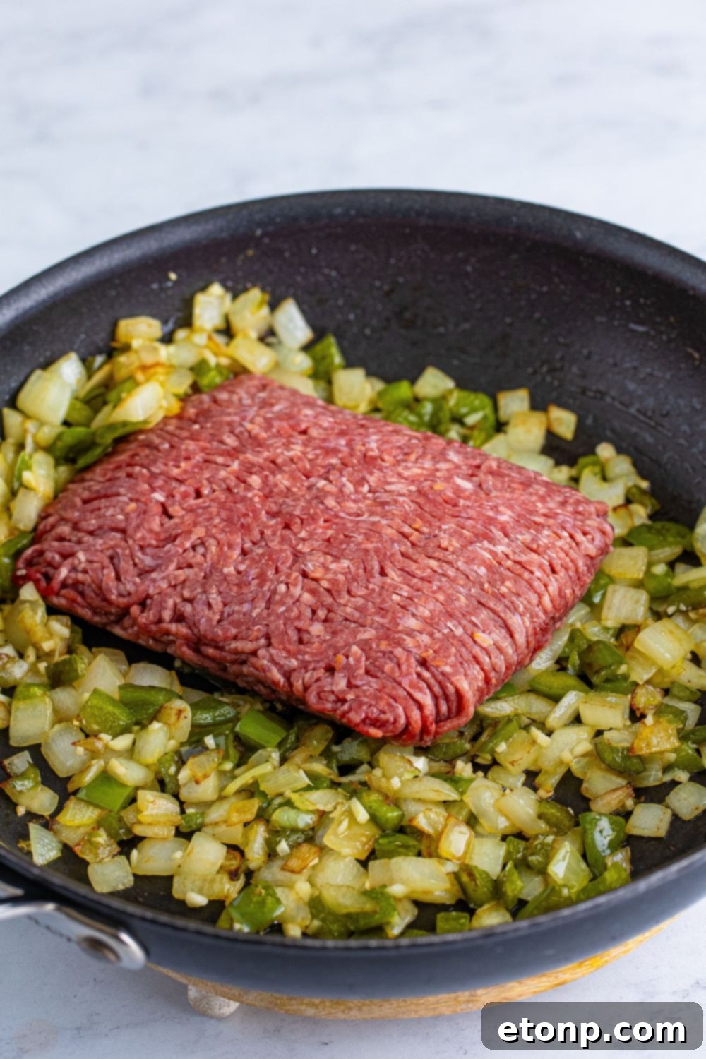 Ground beef browning in a skillet alongside softened onions and peppers, mixing the core ingredients for the Dr. Pepper Sloppy Joes.