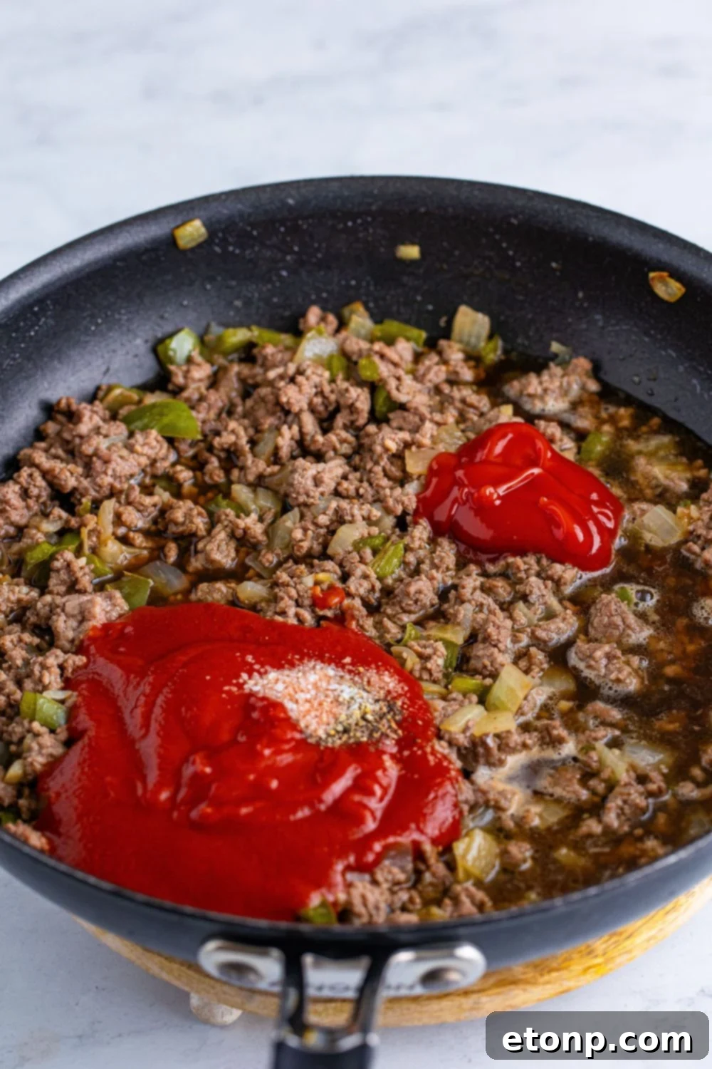 Close-up of seasoning being sprinkled over cooked ground beef in a skillet, preparing for the sauce addition in the Dr. Pepper Sloppy Joes recipe.