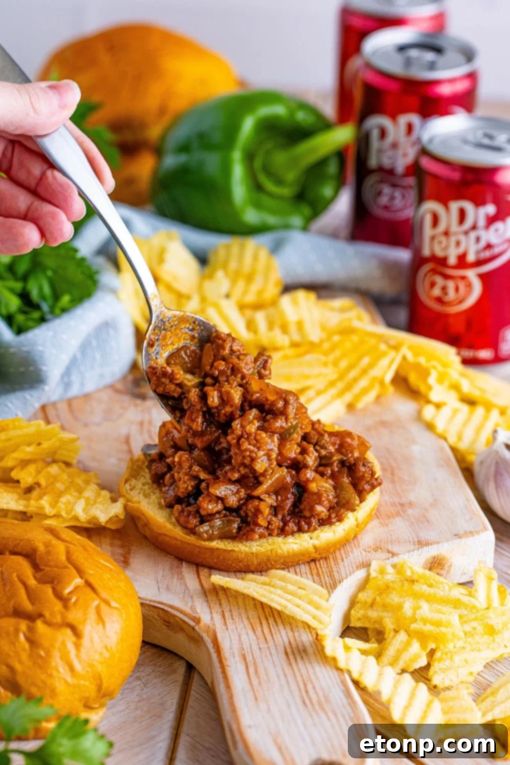 A generous spoonful of Dr. Pepper Sloppy Joe mixture being placed onto a toasted hamburger bun, ready for assembly.