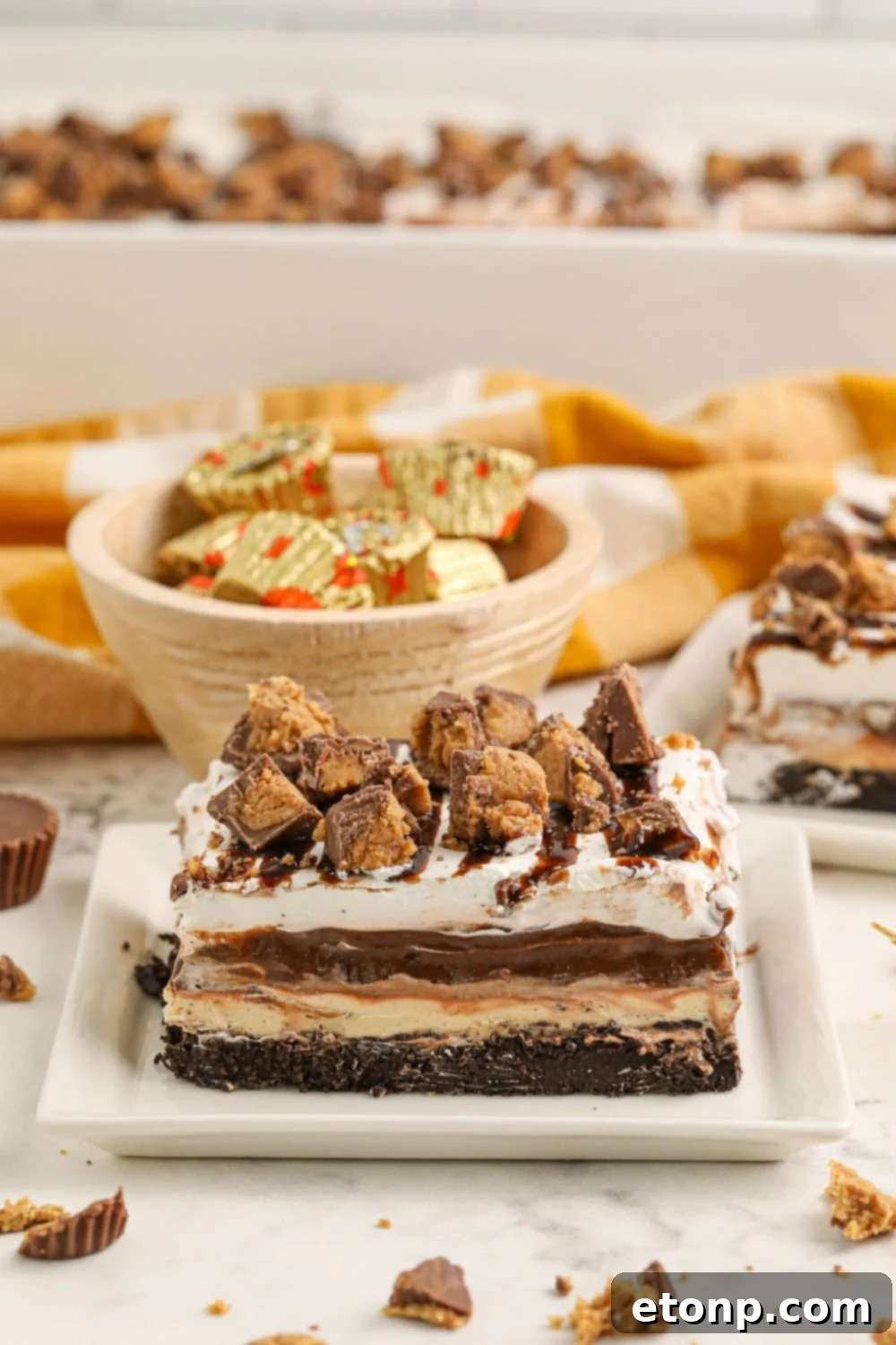 Reese's Peanut Butter Bliss Stack 15 Slices of Reese's Lasagna elegantly arranged on a table, with a bowl of assorted candies and the baking pan visible in the background.