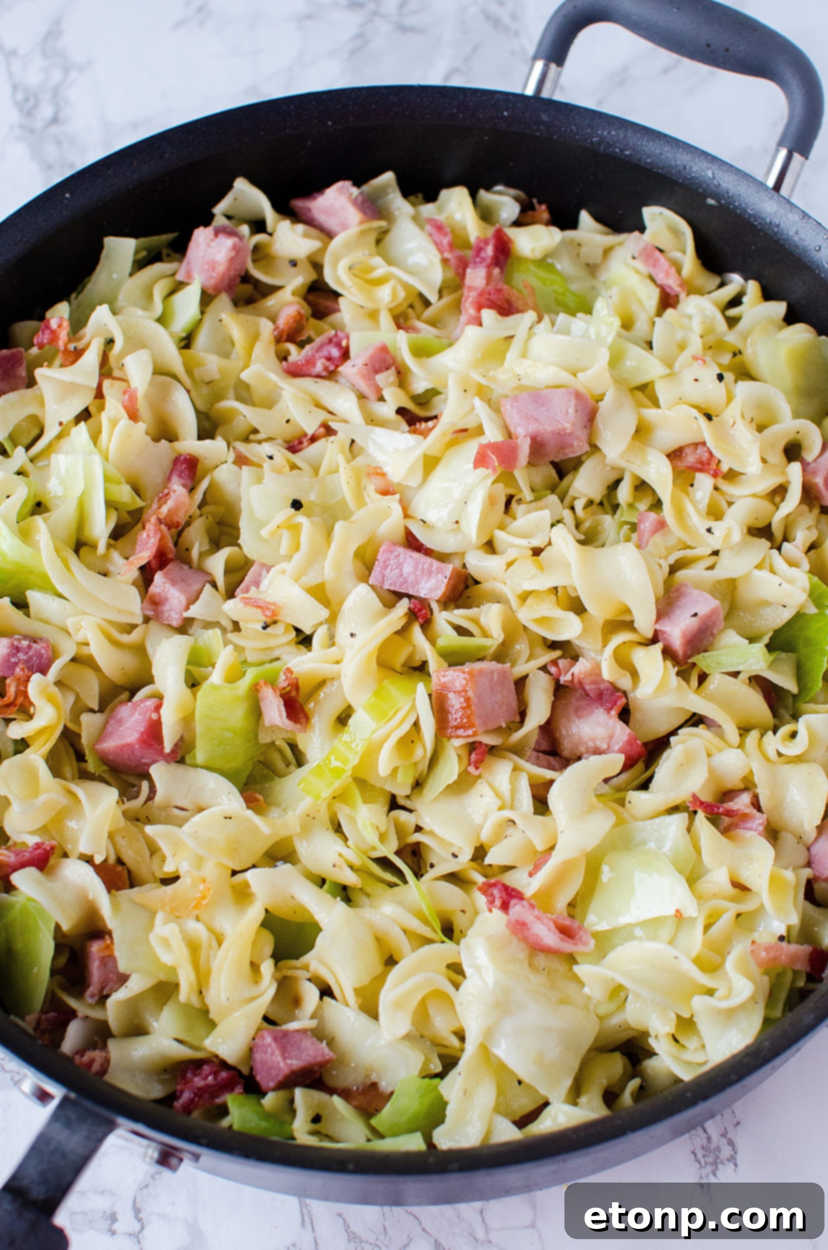 Close-up of a skillet filled with Fried Cabbage, Ham & Noodles (Haluski), showing golden ham and tender cabbage.