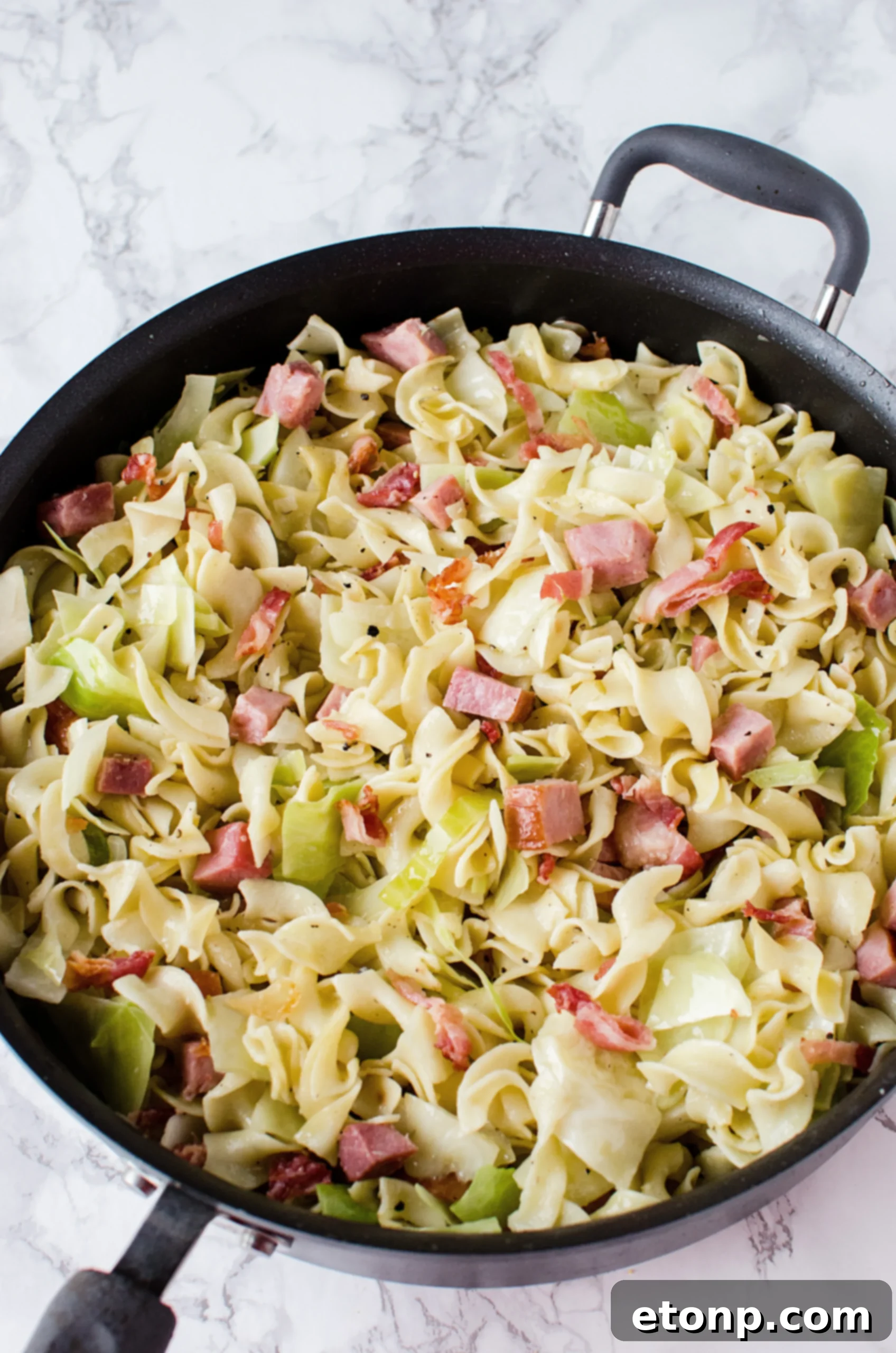A chef gently stirring the cabbage and ham mixture in a skillet.