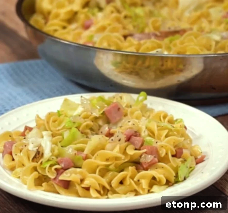 Final plated dish of Fried Cabbage, Ham & Noodles (Haluski) with a fork, ready to eat.