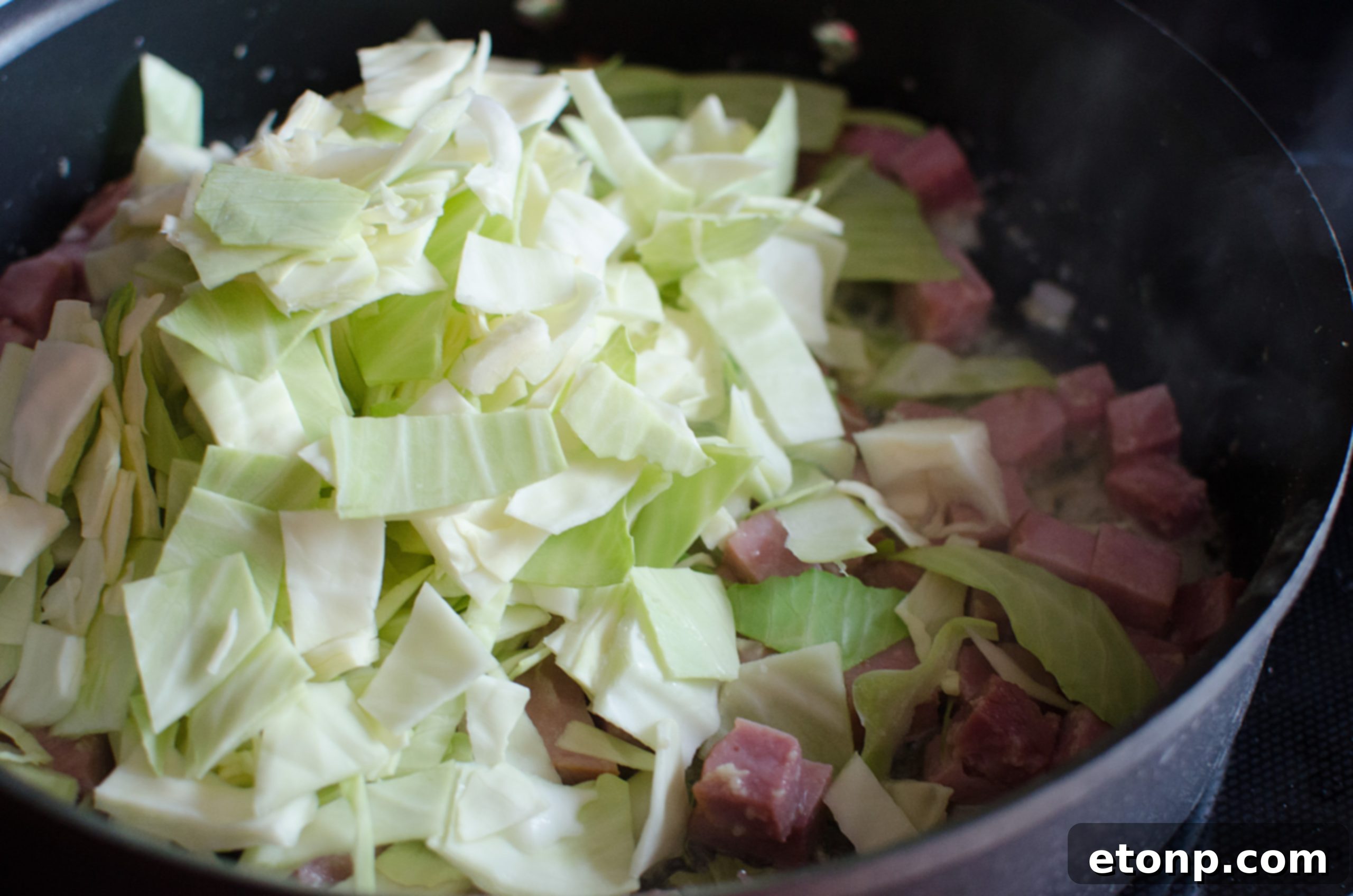 Ingredients laid out on a wooden board, including ham, cabbage, and noodles, ready for cooking.