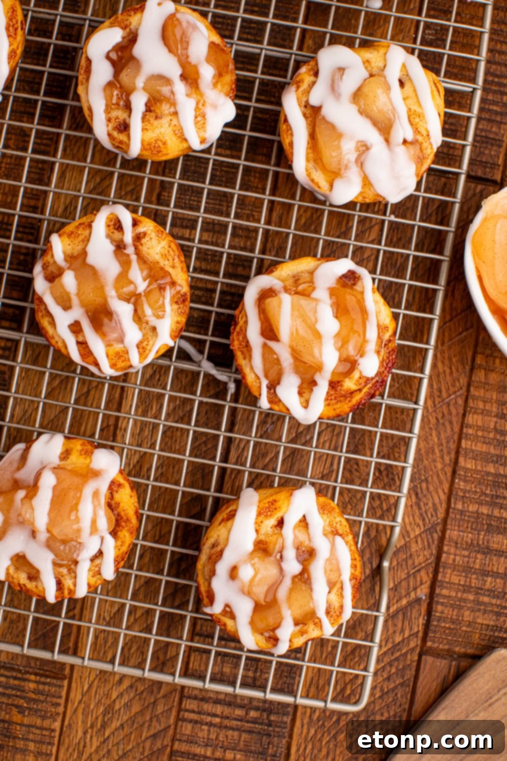 Effortless Apple Tartlets 12 apple cinnamon cups on table on a wire cooling rack with a bowl of pie filling on the side