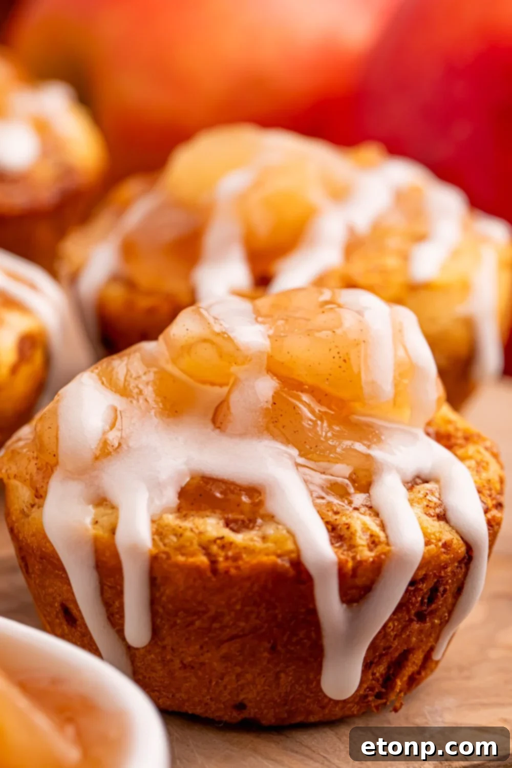 Effortless Apple Tartlets 13 mini apple pies muffin cups on a table with a close up of the icing drizzling down the sides of the cinnamon rolls