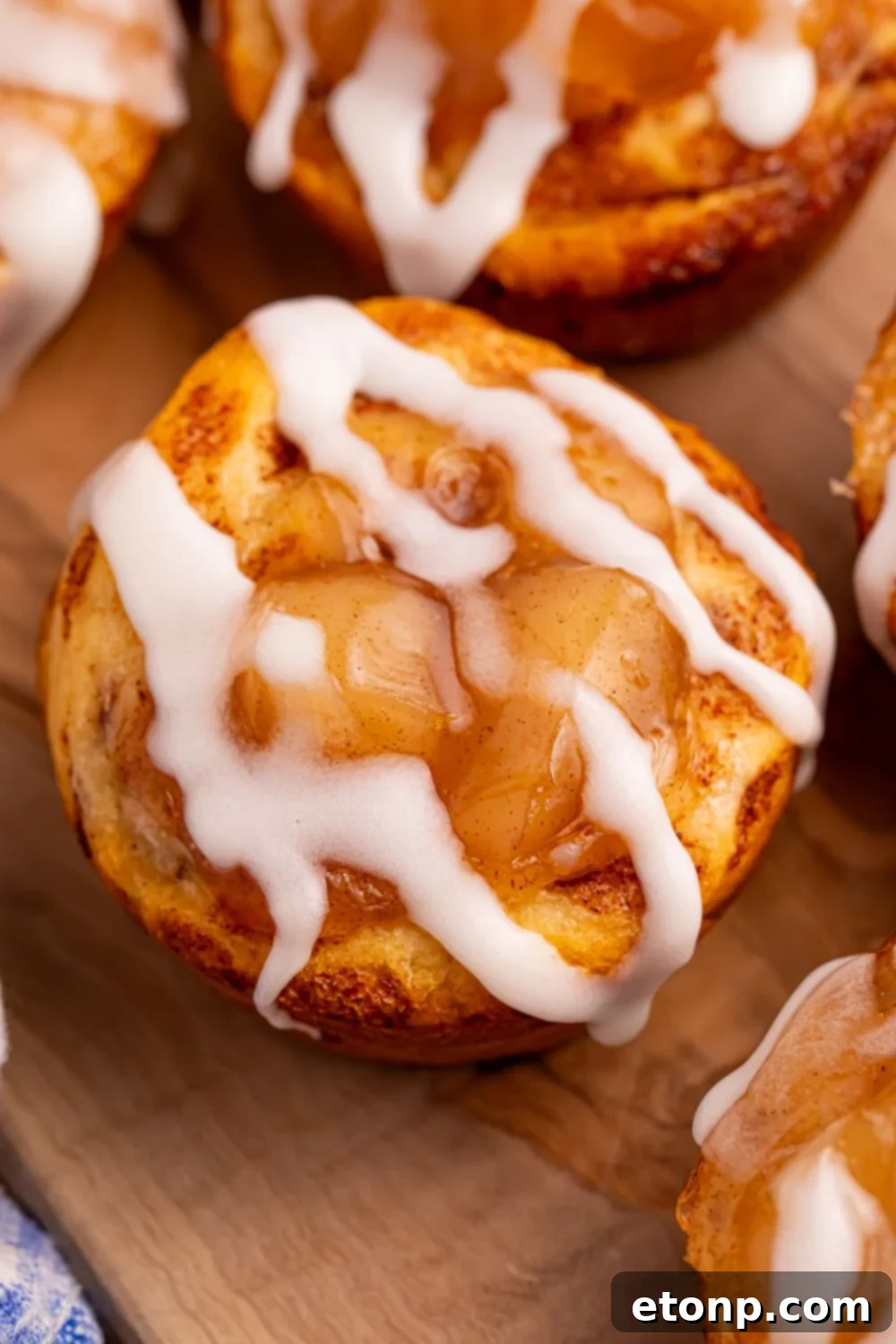 Effortless Apple Tartlets 4 cinnamon rolls with apple pie filling in center and drizzled with icing, sitting on wooden cutting board on table