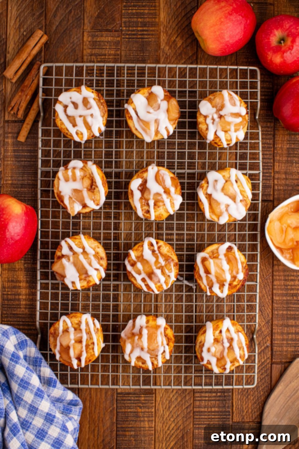 Effortless Apple Tartlets 5 Easy Apple Pie Cups overhead look on table with a cooling rack with rows of apple pie cups on table with apples and cinnamon sticks around the rack