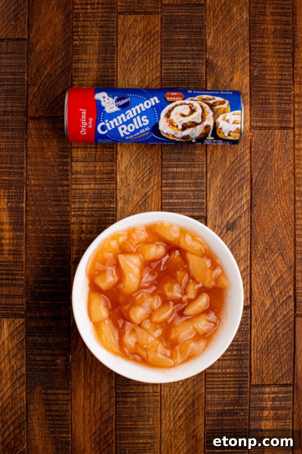 Effortless Apple Tartlets 6 ingredients for apple pie cups on table. Bowl of apple pie filling and a roll of cinnamon rolls on table