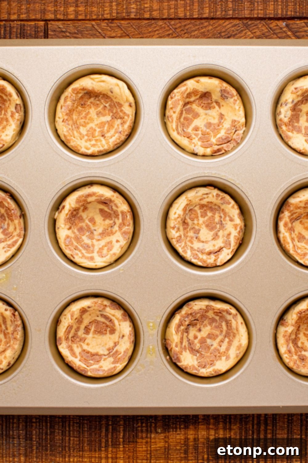 Effortless Apple Tartlets 7 raw cinnamon rolls in a muffin tin with the centers pressed down for the apple pie cups