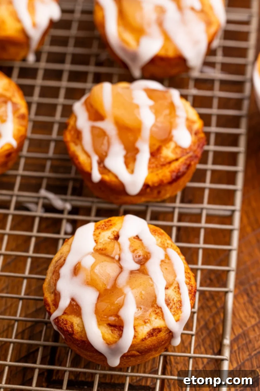 Effortless Apple Tartlets 9 apple pie cups sitting on a wire cooling rack with the glaze drizzled on top