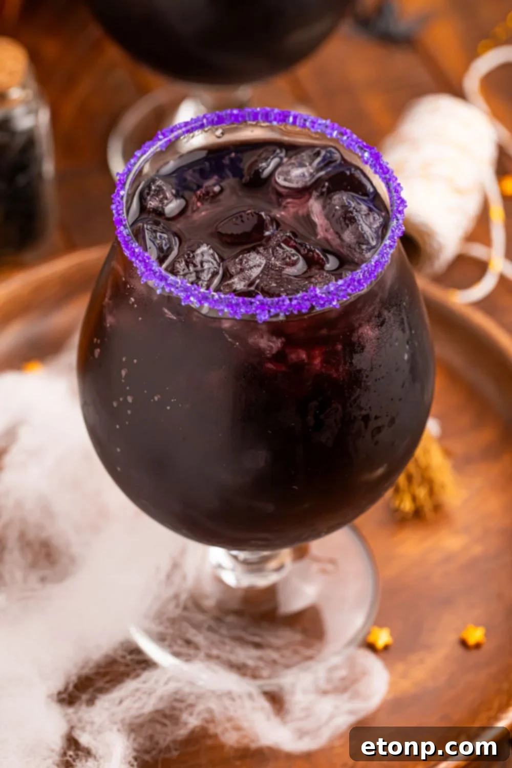 close up of Witches Brew Cocktail in a glass with fake spider web at the bottom of tray with a few candy sprinkles
