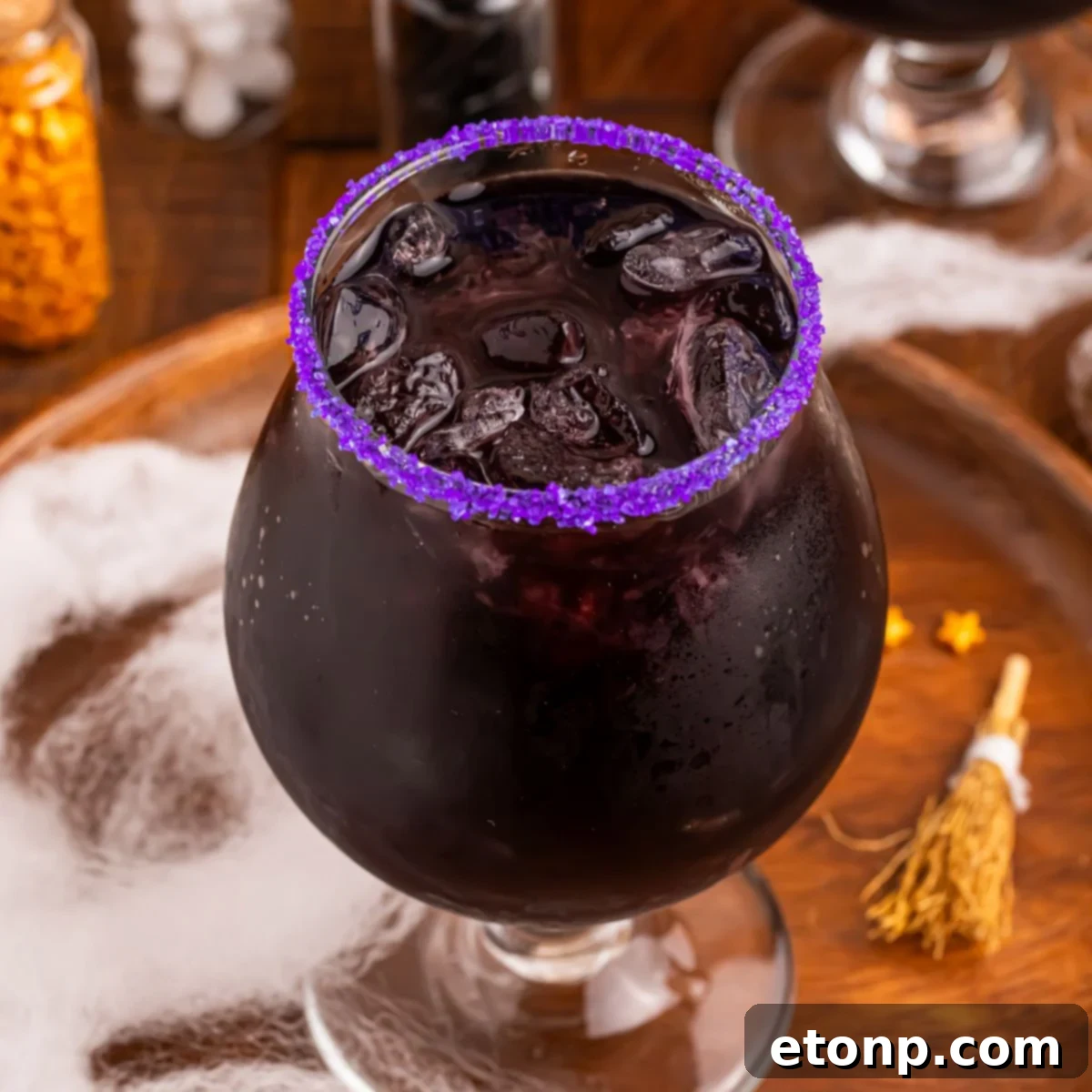 Witches Brew Cocktail sitting on a wooden cutting board with Halloween decor around it on table