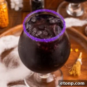 Witches Brew Cocktail sitting on a wooden cutting board with Halloween decor around it on table