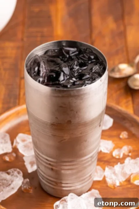 Witches Brew Cocktail mixture in a shaker glass with ice sitting on a tray