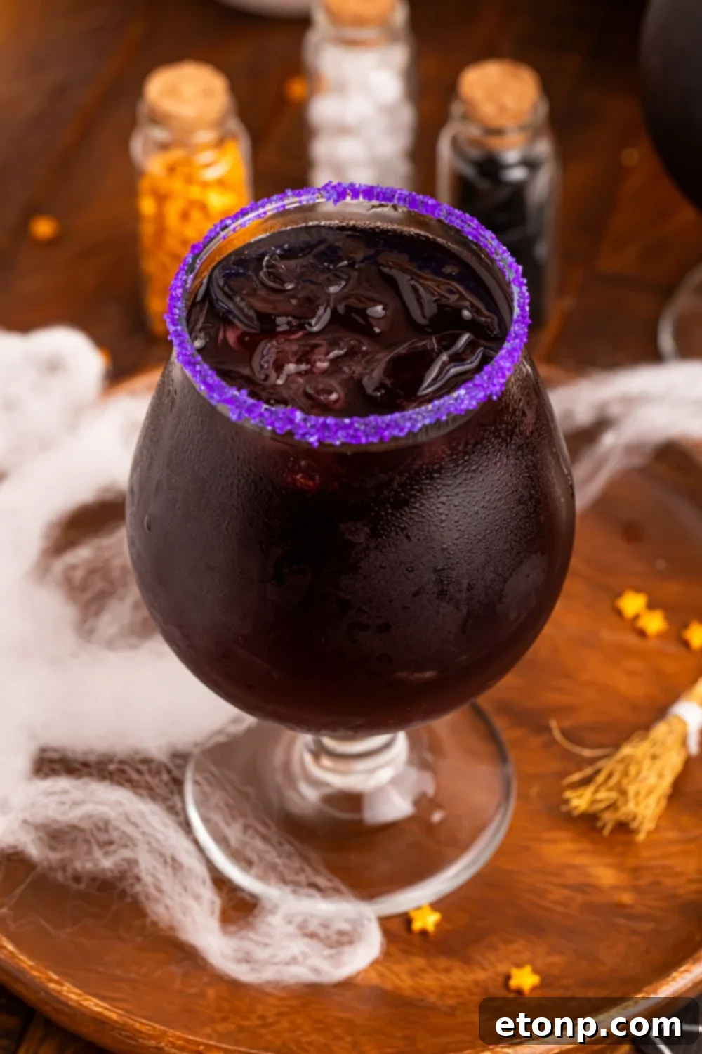 Witches Brew Cocktail on a table with mini bottles of sprinkles in background and fake spiderwebs spread over table for a Halloween vibe