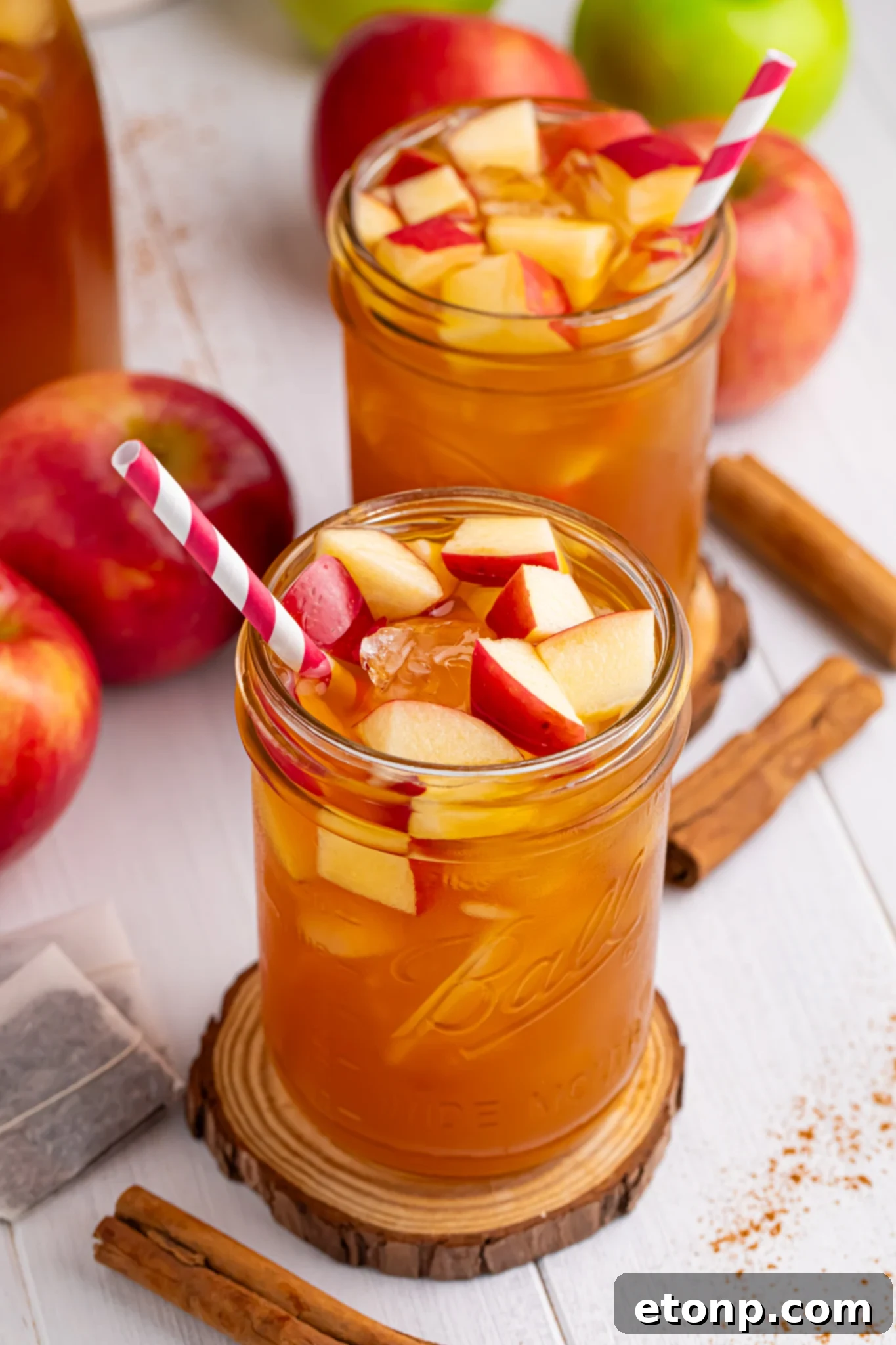 Orchard Apple Iced Tea 2 apple cider iced tea in a glass with a shot of the glass with a straw in it and diced fresh apples with ice cubes