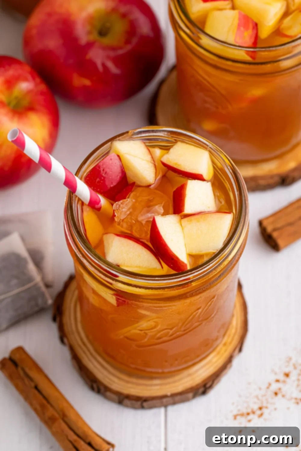 Orchard Apple Iced Tea 11 mason jar with an apple tea sitting on it on a wooden coaster and other glasses and apples spread over the table with a sprinkle of cinnamon on table